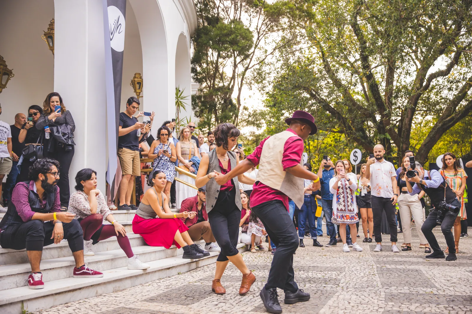 Casal dança em frente à entrada do Nacional Club enquanto o público acompanha a apresentação ao redor. A imagem representa as intervenções artísticas e performances ao vivo distribuídas pelos ambientes da Jazz Mansion.
