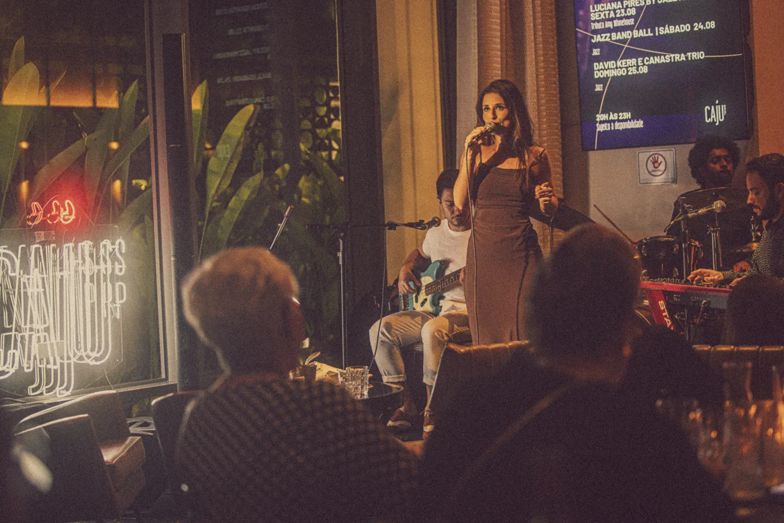 Cantora no palco do Caju, com público próximo e iluminação acolhedora.