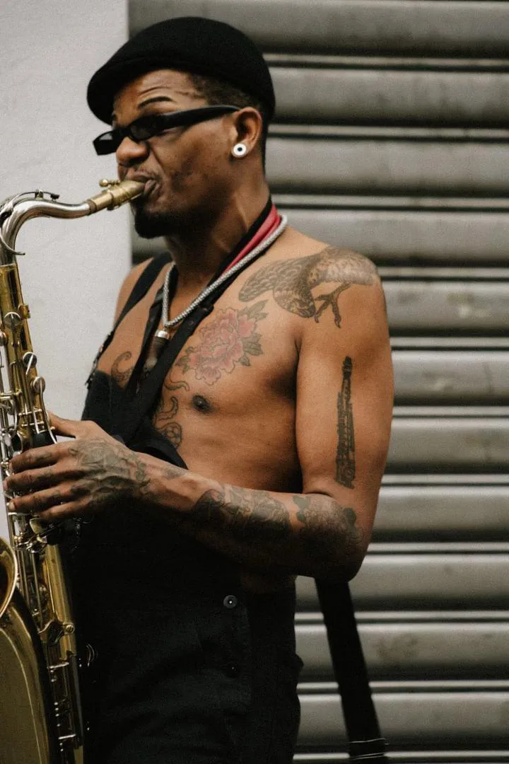 Vinícius Chagas toca saxofone usando chapéu e óculos.